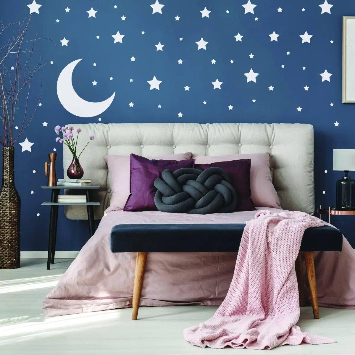 Cozy bedroom with white star wall decals and crescent moon on blue wall, featuring plush bedding and decor.