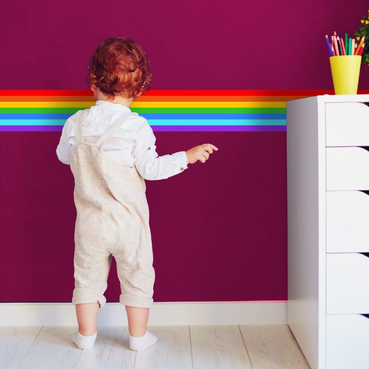 Child admiring a vibrant rainbow spectrum wall decal on a purple wall, brightening up the nursery decor.