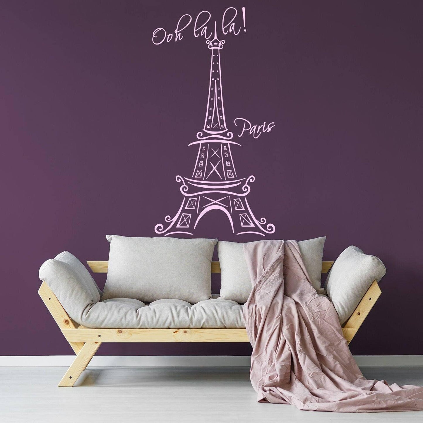 Eiffel Tower wall decal with 'Oh la la!' text on purple wall above a cozy couch with a blanket.