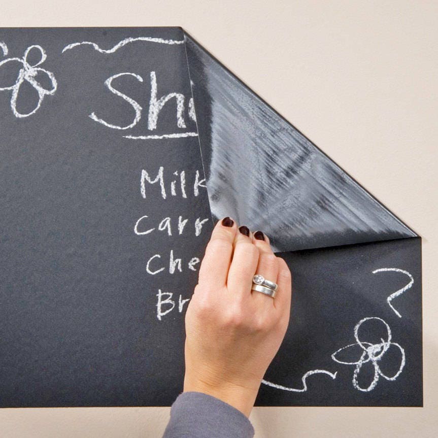 Hand peeling a chalkboard wall decal showing scribbled grocery list and doodles.