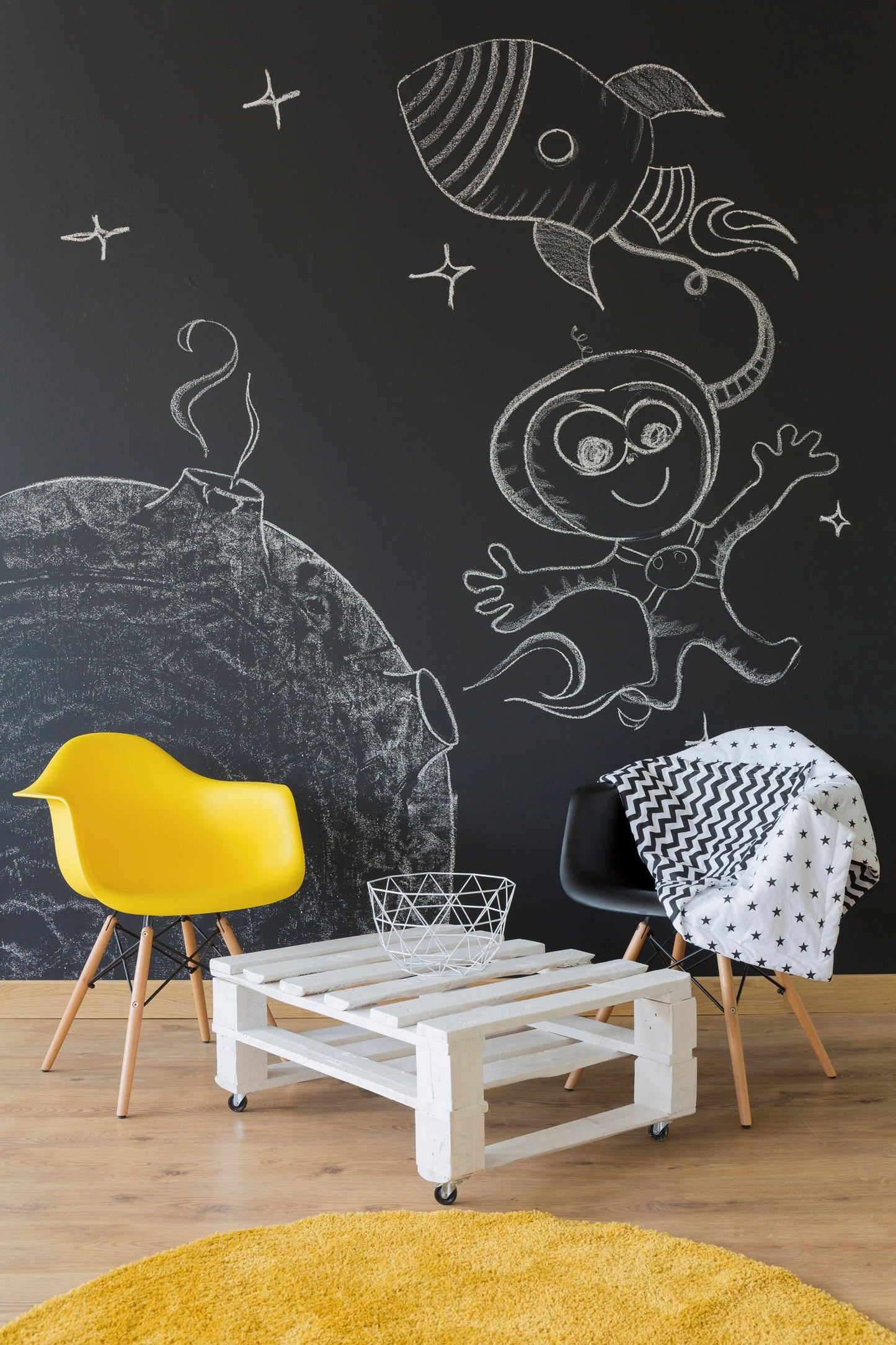 A cozy kids playroom featuring a black chalkboard wall with playful drawings of a rocket and an astronaut.