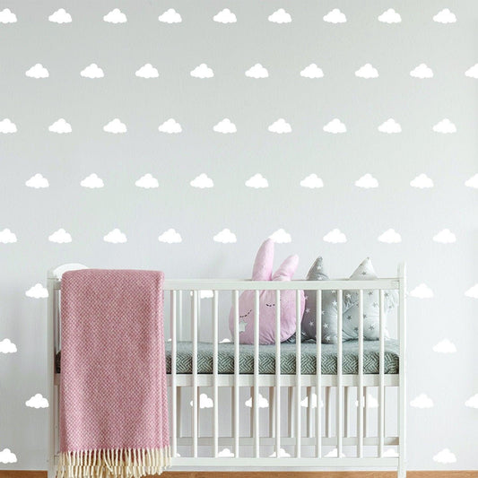 Nursery with white cloud wall decals above a crib featuring pink and gray plush toys and a cozy blanket.